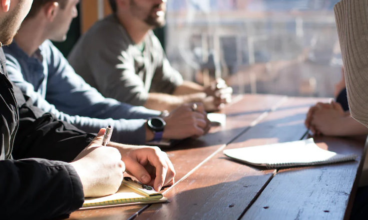 People sitting at a table with pen and paper People sitting at a table with pen and paper